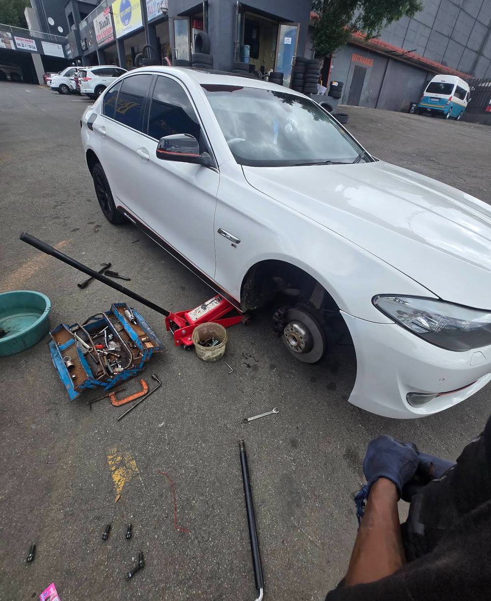 White BMW on a trolley jack with the front wheel removed and tools laid out on the forecourt